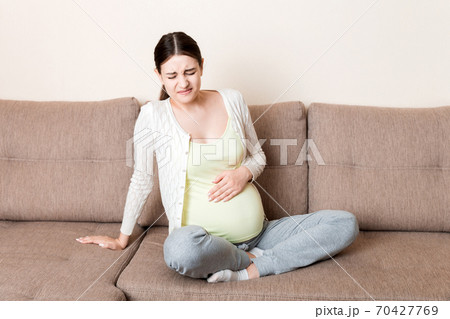 Pregnant woman with painful belly on sofa at home Pregnant woman with painful belly on sofa at home 70427769