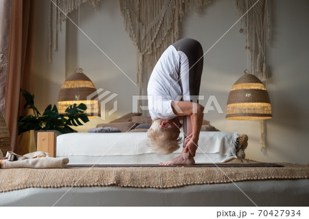 Attractive senior woman working out standing in Uttanasana at home. Attractive senior woman working out standing in Uttanasana at home. 70427934