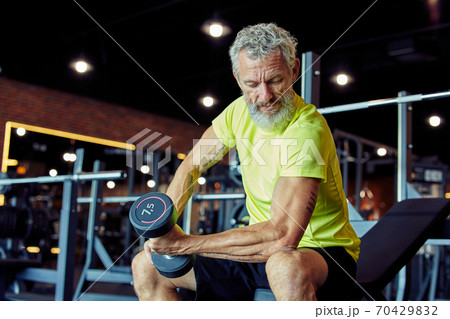 Weight workout. Focused mature man in sportswear lifting heavy dumbbells and pumping his biceps while training at gym Weight workout. Focused mature man in sportswear lifting heavy dumbbells and pumping his biceps while training at gym 70429832