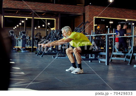 Warming up before training. Full length of a mature caucasian man in sportswear working out at gym, doing squats Warming up before training. Full length of a mature caucasian man in sportswear working out at gym, doing squats 70429833