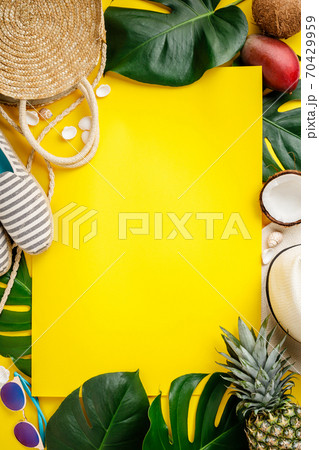 Straw hat, camera, bag, summer shoes, sunglasses, shells, tropical leaves and fruits over yellow background 70429959
