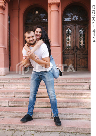 Beautiful gilr climbed on her boyfriend back and hug him. Happy smiled couple spend time in city 70432225