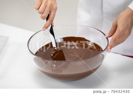 hand of Female Confectioner close up mixes melted swiss chocolate in glass bow hand of Female Confectioner close up mixes melted swiss chocolate in glass bow 70432430