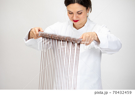 Attractive Female chocolatier pouring excess melted dark chocolate from molds 70432459