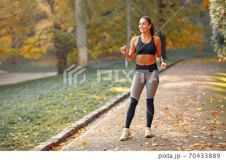 Sports girl in a black top training in a autumn park 70433889
