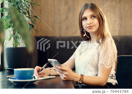 Young business woman sitting at the table in a coffee shop and making notes 70443784