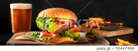 Burger and beer panorama. Hamburger with beef, cheese, onion, tomato, and green salad, with pickles and French fries, a side view 70447406