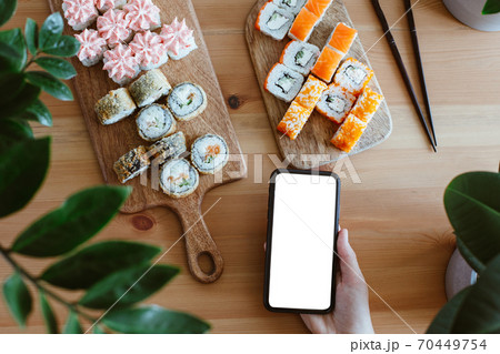 Japanese home delivery kitchen, rolls and mobile phone with white screen in hand on a wooden background 70449754