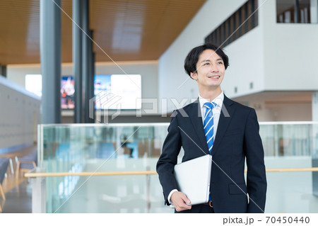 ターミナルでノートパソコンを持って立つ若いビジネスマン ターミナルでノートパソコンを持って立つ若いビジネスマン 70450440