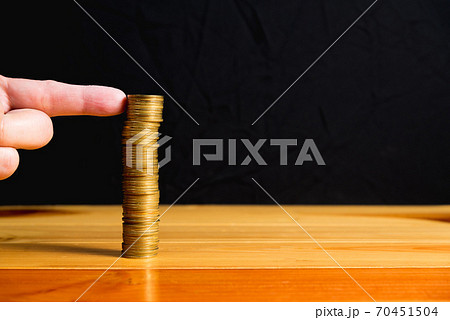 Finger pushing a column of coins on wooden table with black wall, gold coins falls , business crisis concept. shallow focus Finger pushing a column of coins on wooden table with black wall, gold coins falls , business crisis concept. shallow focus 70451504