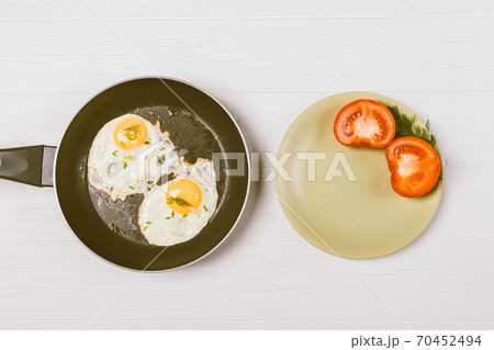 Top view of fried eggs in frying pan next to plate with tomato slices Top view of fried eggs in frying pan next to plate with tomato slices 70452494