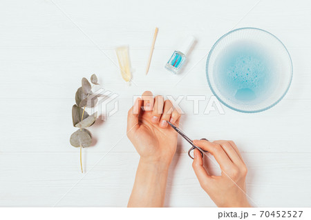 Flat lay female hands doing manicure at home using scissors Flat lay female hands doing manicure at home using scissors 70452527