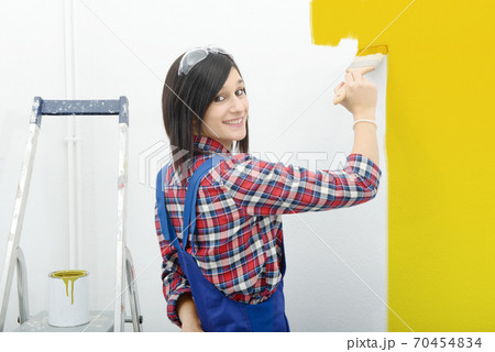 pretty young woman paints the wall yellow color 70454834