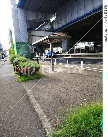 工事中の高速道路の高架下、バス停に放置された自転車、車道を挟んだフェンスの向こうには撤去自転車保管所 70458186