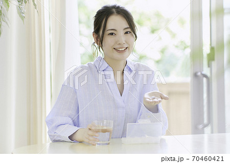 リビングで薬を飲もうとしている若い女性　 70460421