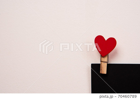 Wooden clothespin with a red heart on a black sheet of paper and a light background 70460789