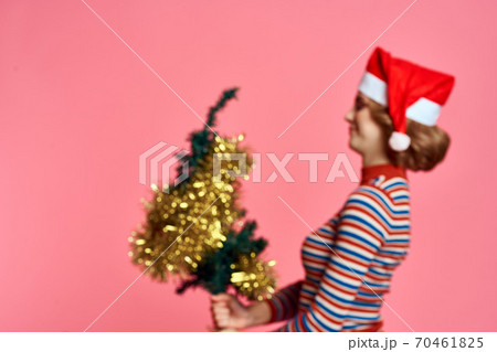 Woman with a Christmas tree in her hands and yellow shiro red cap pink background Woman with a Christmas tree in her hands and yellow shiro red cap pink background 70461825