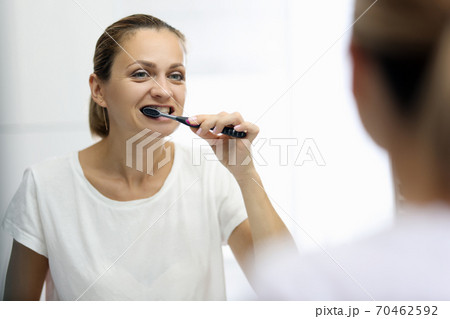 Woman in awhite T-shirt is brushing her teeth in front of mirror 70462592