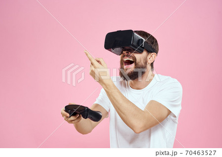 Man in virtual reality glasses joystick playing video lifestyle white t-shirt pink background Man in virtual reality glasses joystick playing video lifestyle white t-shirt pink background 70463527