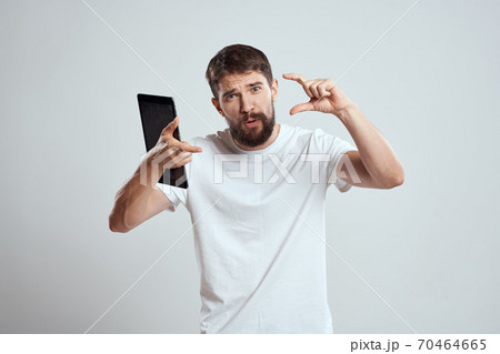 A man in a white T-shirt with a tablet in his hands emotions technology light background A man in a white T-shirt with a tablet in his hands emotions technology light background 70464665
