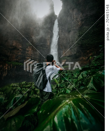 A guy standing in front of a massive waterfall A guy standing in front of a massive waterfall 70465548