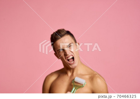 Handsome man with massager in hand on isolated pink background cropped view clean skin Handsome man with massager in hand on isolated pink background cropped view clean skin 70466325