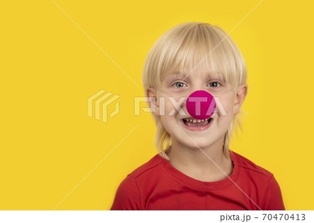 Cute blond boy wears clown nose and smiling. Portrait child close up on yellow background Cute blond boy wears clown nose and smiling. Portrait child close up on yellow background 70470413