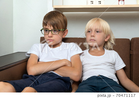 Two friends are sitting on couch and are looking at something. Two brothers at home on couch Two friends are sitting on couch and are looking at something. Two brothers at home on couch 70471117