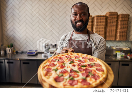 Joyful Afro American man holding wooden board with pizza Joyful Afro American man holding wooden board with pizza 70475431