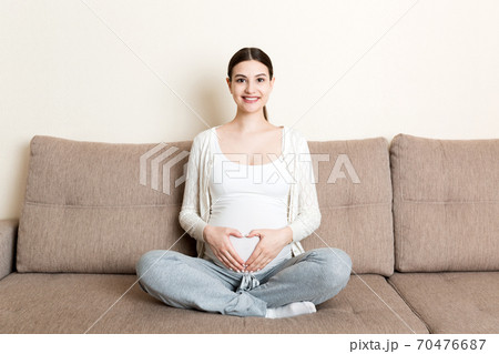 photo of cute caucasian future mom lying in light living room on sofa and holding hands on tummy photo of cute caucasian future mom lying in light living room on sofa and holding hands on tummy 70476687