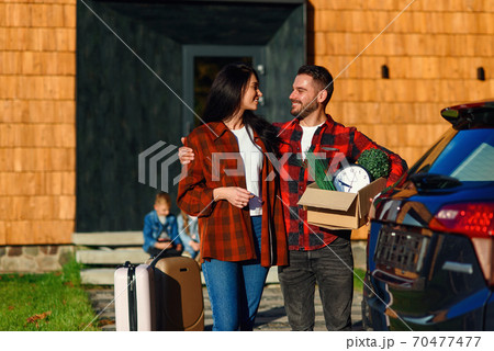 Adorable couple in love looking to each other standing near modern house with carton box during moving to the new house. 70477477