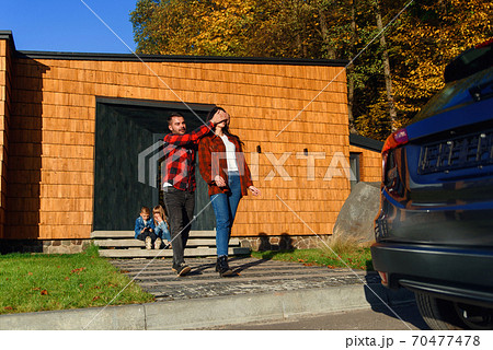 Happy man closes his wife's eyes with his hands and leads her to a new black car. Present for woman. 70477478