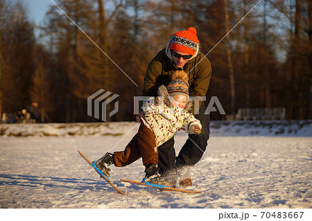 Young man learning his small child to ski. Smiling boy almast falling. Sunny photo on background of winter snowy park 70483667