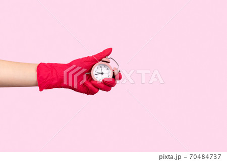Female hand in a rubber glove holding alarm clock on pink background Female hand in a rubber glove holding alarm clock on pink background 70484737