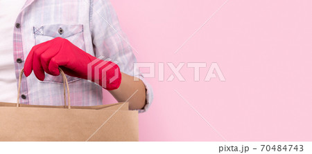 Womans hand in a rubber glove holding paper bag on pink background 70484743