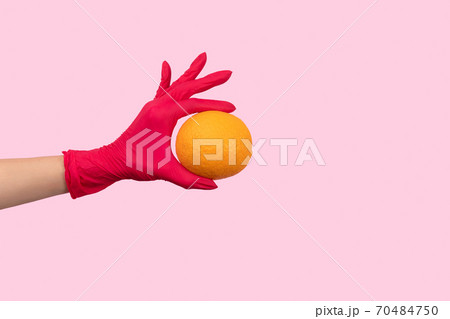 Womans hand in a pink glove holding orange 70484750