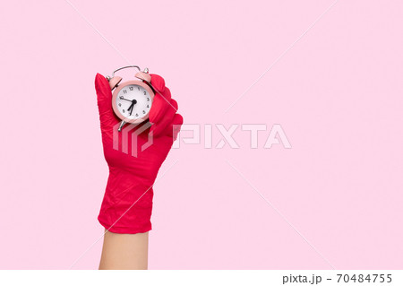 Female hand in a rubber glove holding alarm clock on pink background Female hand in a rubber glove holding alarm clock on pink background 70484755