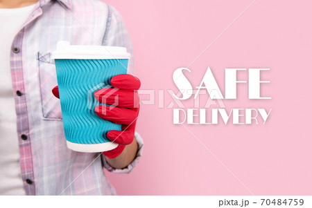 Female hand in a rubber glove holding blue paper cup on pink background Female hand in a rubber glove holding blue paper cup on pink background 70484759