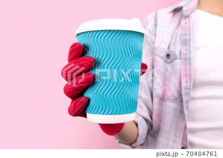 Female hand in a rubber glove holding blue paper cup on pink background Female hand in a rubber glove holding blue paper cup on pink background 70484761