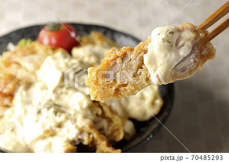 ミニトマトなど野菜も一緒に乗っているタルタルソースたっぷりのチキン南蛮丼の一切れを箸でつまんで食べる 70485293