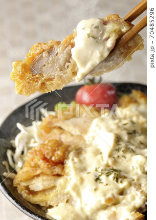 ミニトマトなど野菜も一緒に乗っているタルタルソースたっぷりのチキン南蛮丼の一切れを箸でつまんで食べる ミニトマトなど野菜も一緒に乗っているタルタルソースたっぷりのチキン南蛮丼の一切れを箸でつまんで食べる 70485296