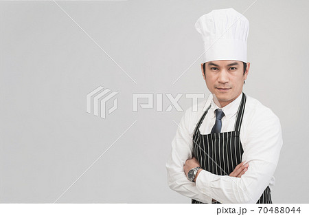Portrait of young Asian male chef looks straight to the camera isolated in grey background with copy space, concept portrait of cook, chef profession. Portrait of young Asian male chef looks straight to the camera isolated in grey background with copy space, concept portrait of cook, chef profession. 70488044