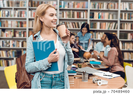 Young girl drinks coffee while standing in library 70489460