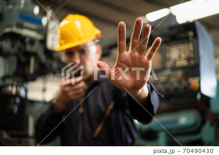 Selective focus of industrial worker in factory site gesture keep out while communicating with a walkie talkie, concept restricts access in industrial factory, working profession, factory restriction 70490430