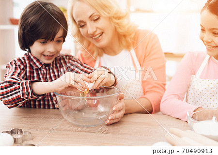 Grandson helps grandmother break eggs for cooking. 70490913