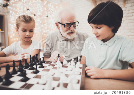 Children and grandpa are playing chess. Children and grandpa are playing chess. 70491386