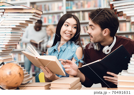 A girl looks at a guy while reading a book. A girl looks at a guy while reading a book. 70491631