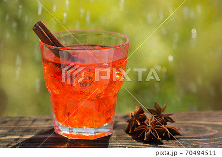 in a glass of colored soda water and a stick of cinnamon, against a background of greenery, drops of water in a glass of colored soda water and a stick of cinnamon, against a background of greenery, drops of water 70494511