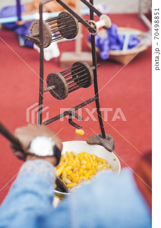 Weaver digests cocoons of silkworm butterflies and spins one thread from them. Manual production of silk fabric using old traditional devices. Bangkok, Thailand. 70498851