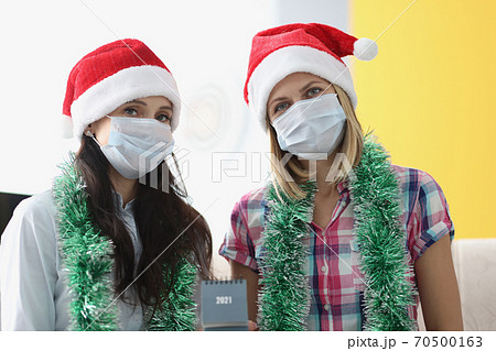Two woman in protective mask sit side by side and hold 2021 calendar. Two woman in protective mask sit side by side and hold 2021 calendar. 70500163